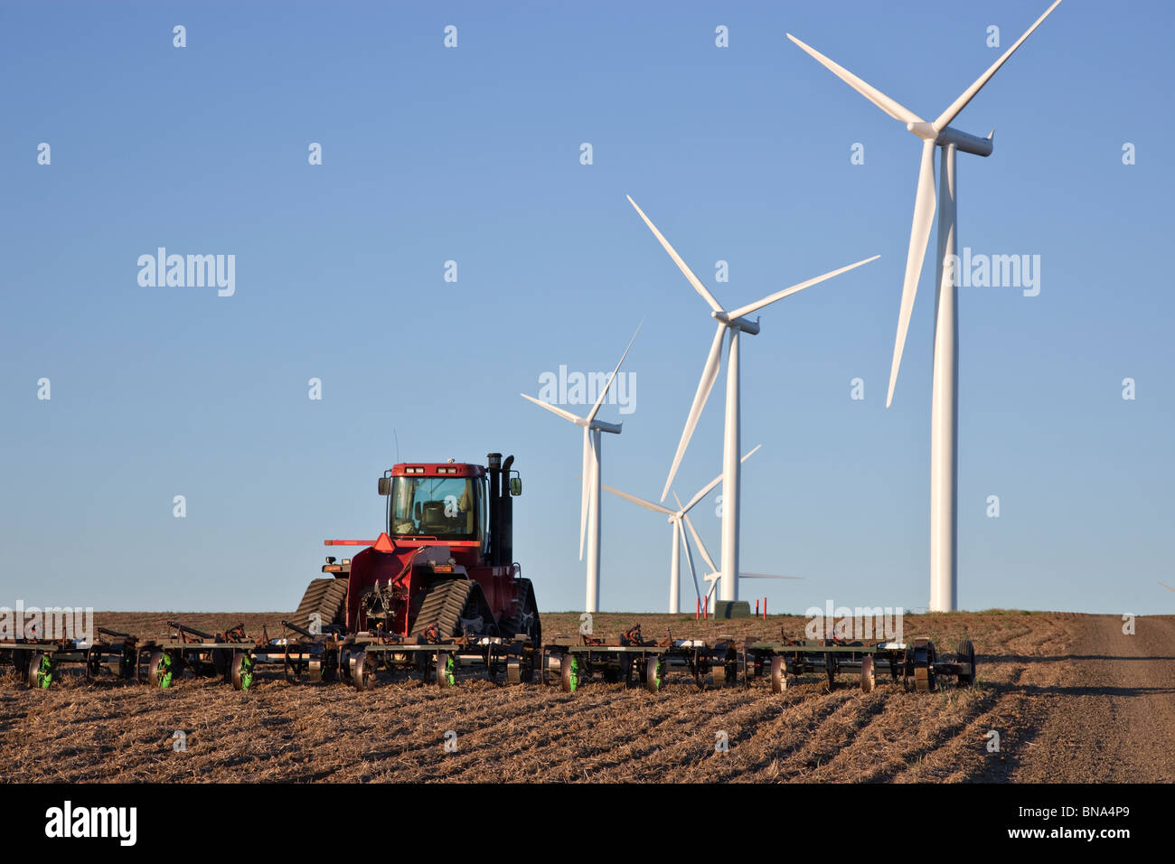 Il trattore trascinando harrow, maggese campo di grano, wind farm. Foto Stock