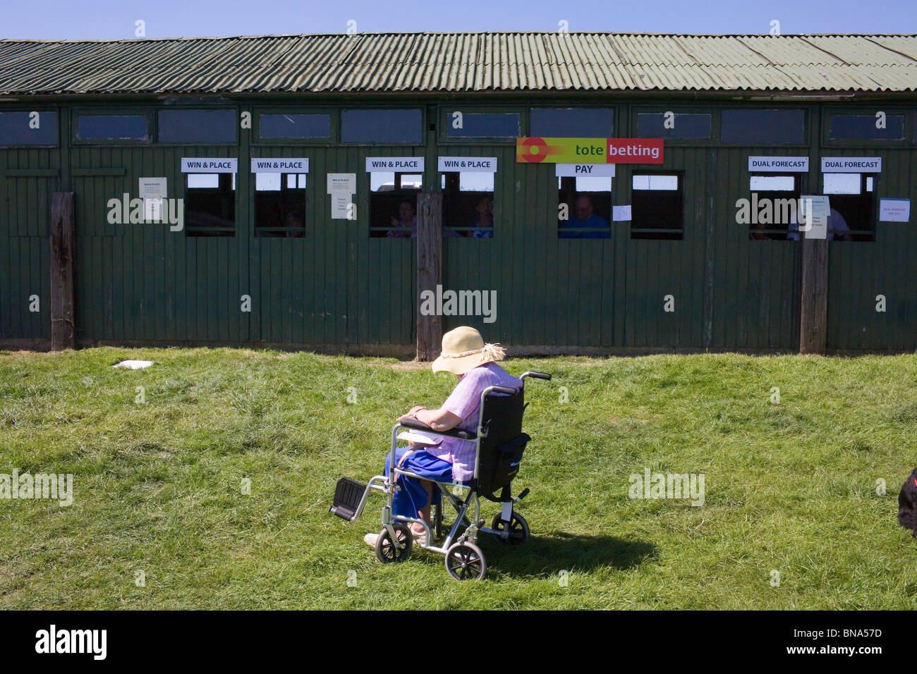 Una donna anziana in una sedia a rotelle si siede da la tote in una calda giornata estiva nella campagna inglese. Foto Stock