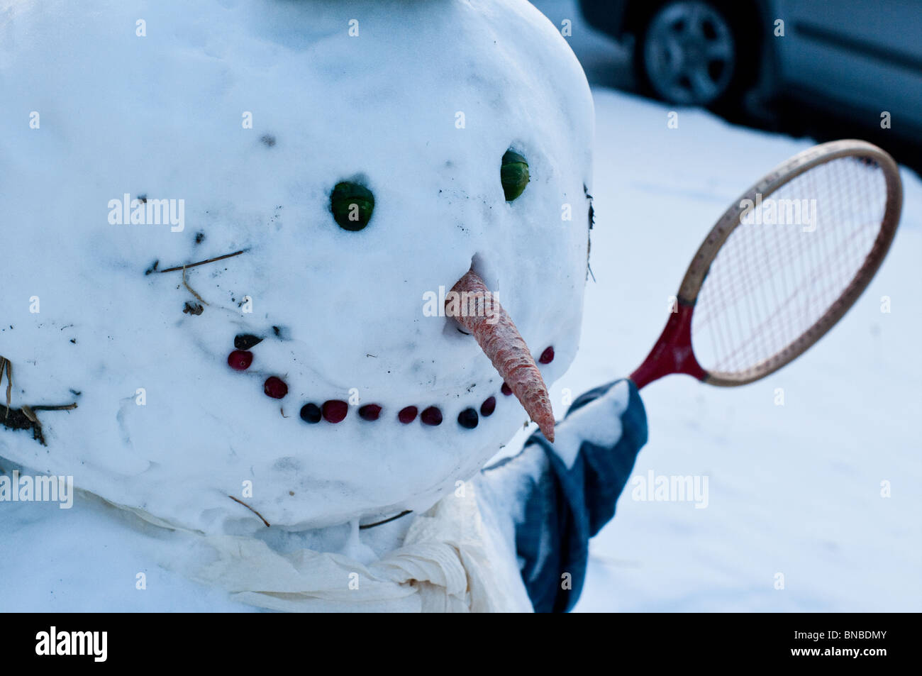 Un pupazzo di neve con una racchetta da tennis per un braccio è raffigurato vicino fino in una fredda giornata invernale e. Foto Stock