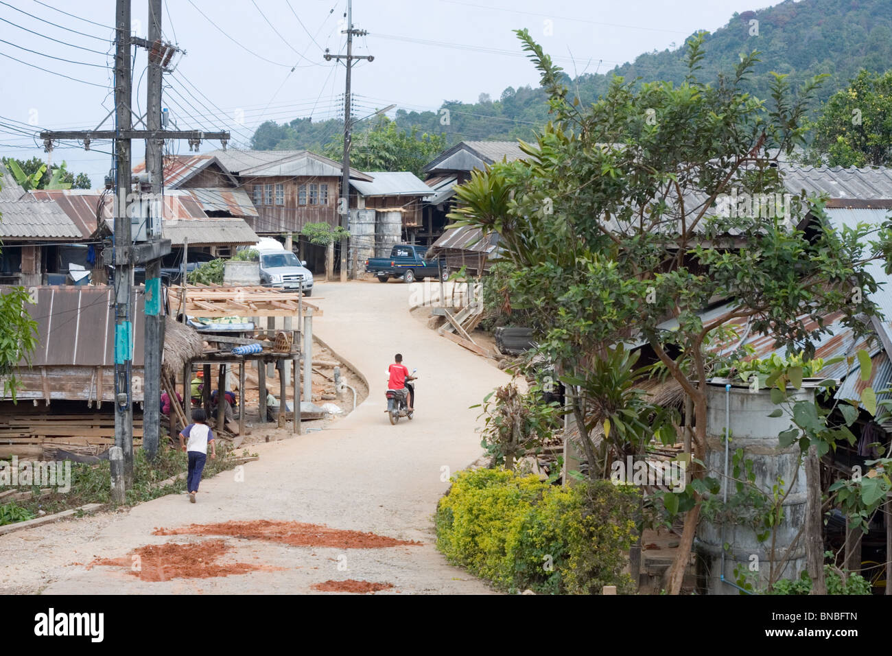 Un uomo su una moto a cavallo di un tipico villaggio thailandese, vietare la fino, Mae Hong Son Provincia, Thailandia Foto Stock