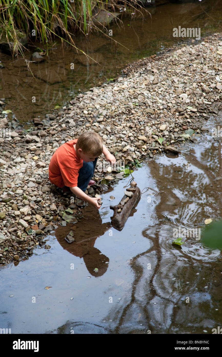 Piccolo Ragazzo contemplando le pietre accanto al fiume Alyn. Foto Stock