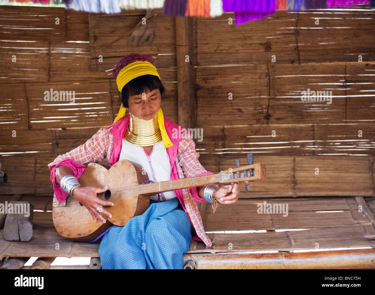 Una donna dalla Padaung lungo collo della tribù della collina di suonare una chitarra vicino a Tha Ton, Chiang Mai Provincia, Thailandia Foto Stock