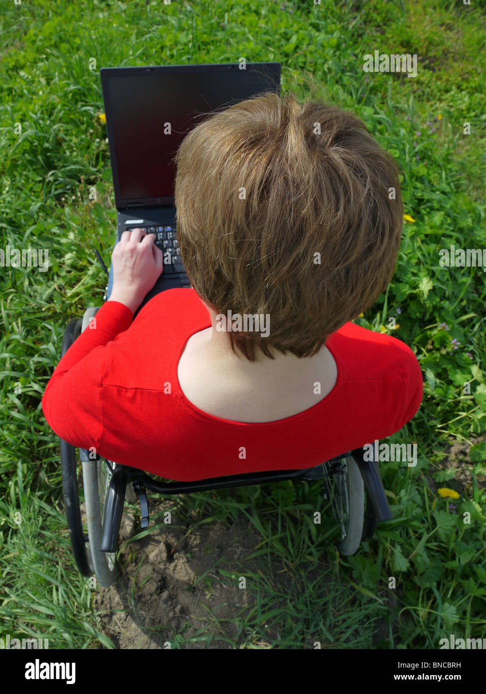 Donna disabile su sedia utilizzando laptop all'aperto Foto Stock