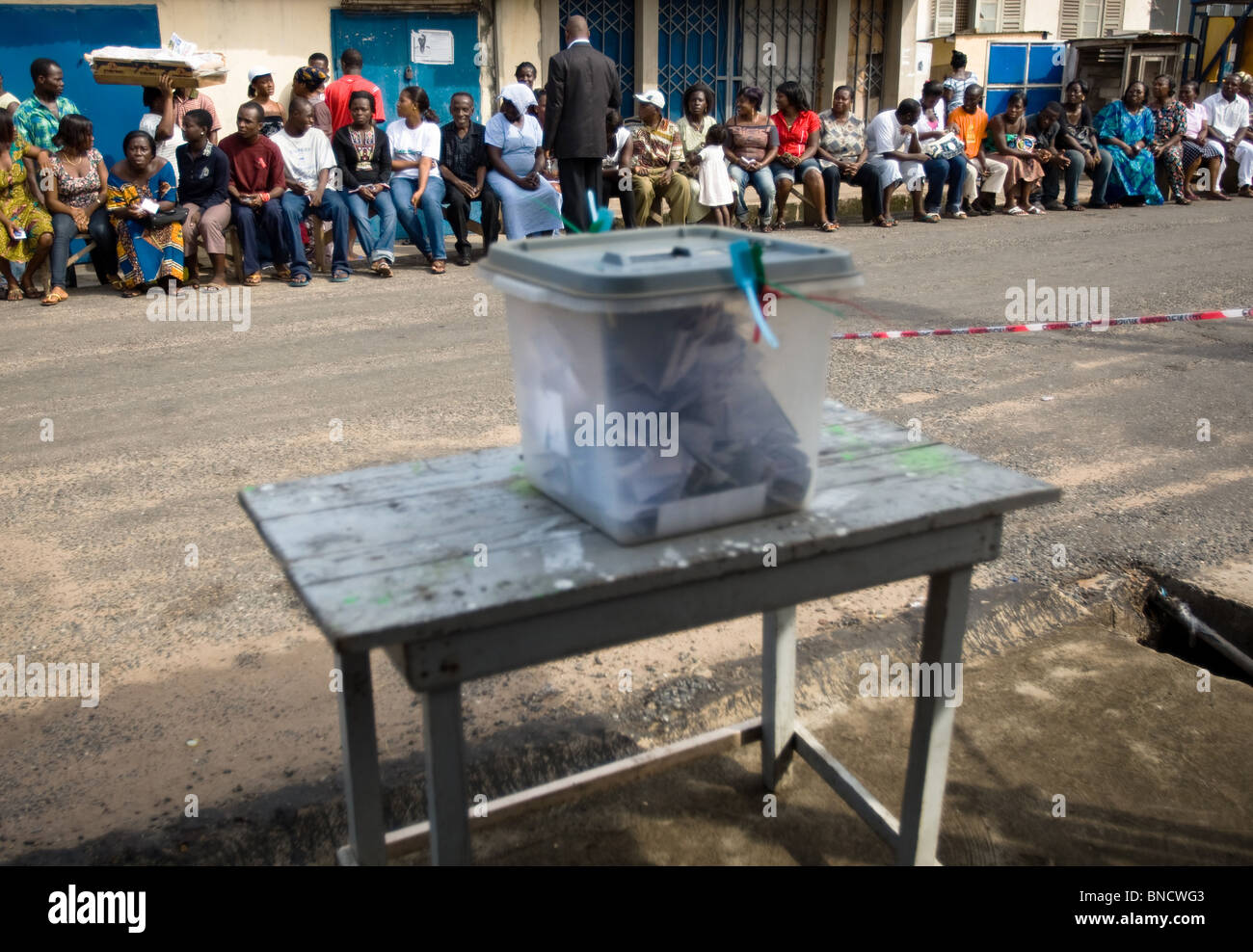 Persone a sedersi su una panchina in strada in attesa di votare in corrispondenza di una stazione di polling nella capitale Accra durante le elezioni presidenziali Foto Stock