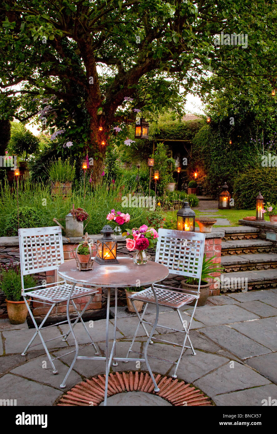 Tavolo in metallo e sedie sul patio con candele e fanali in giardino di notte Foto Stock