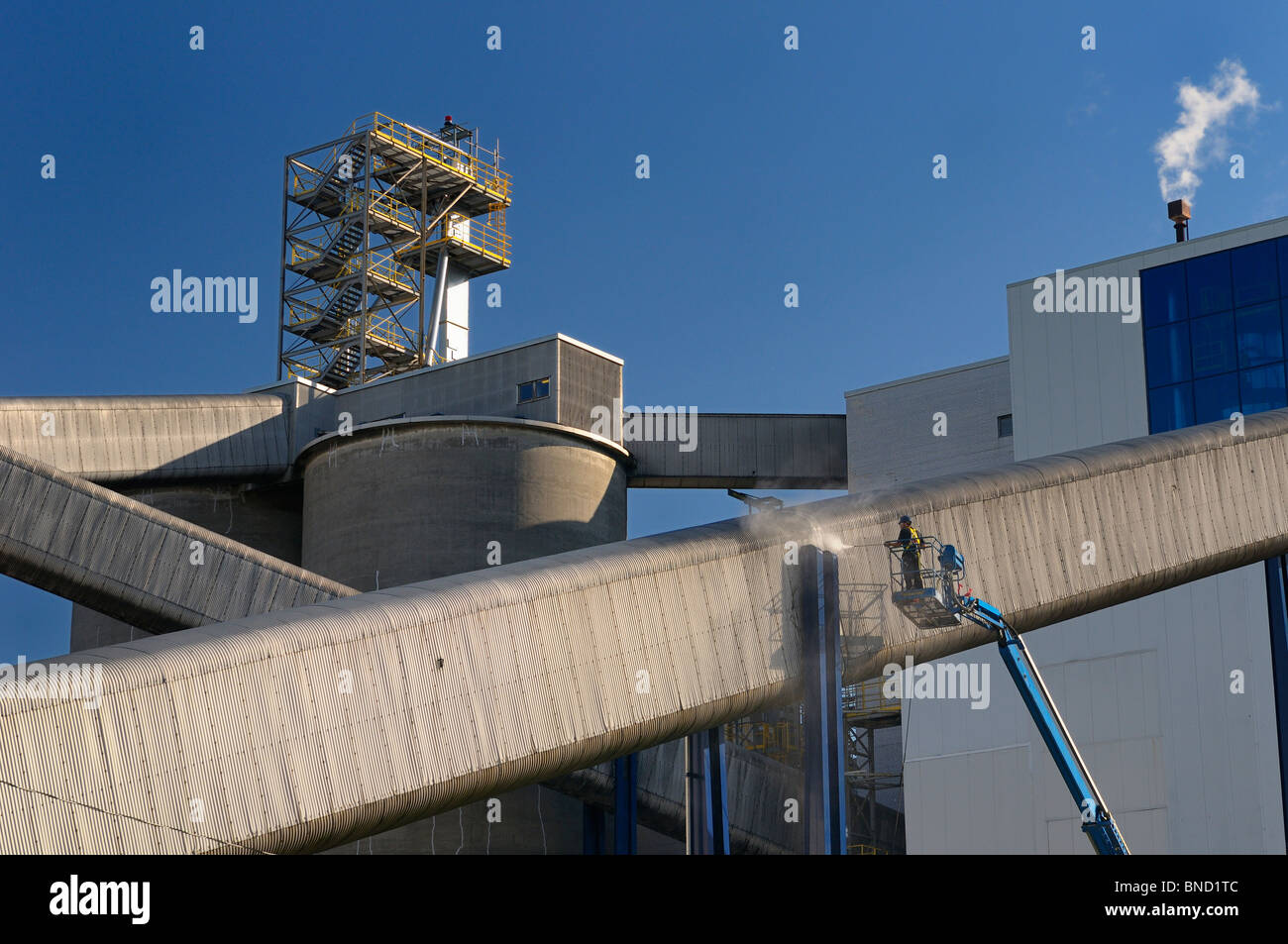 Lavoratore su di un braccio di sollevamento del carrello di alimentazione un lavaggio esterno dello scivolo convogliatore in un complesso industriale contro un cielo blu toronto Foto Stock