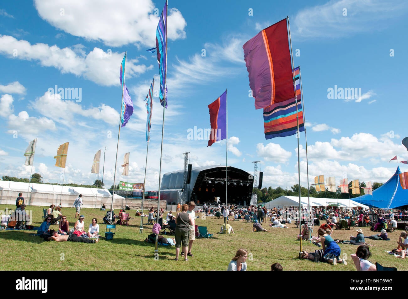 Le bandiere e la folla davanti al palco principale al Womad Festival musicale con cielo blu e soffici nuvole bianche Foto Stock