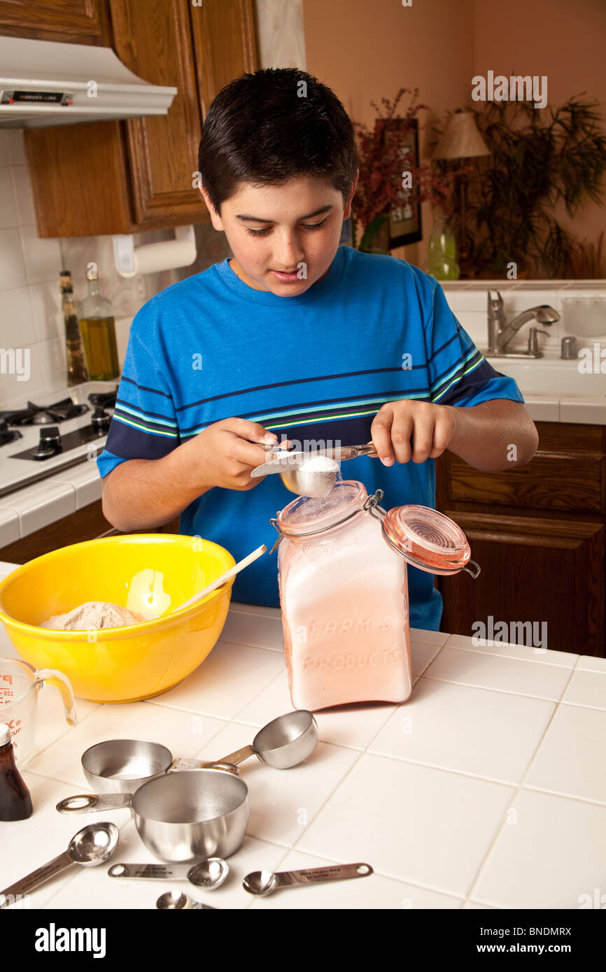 12-14 anni etnia ispanica diverse ragazzo in maglietta blu misurare gli ingredienti della cucina.POV Stati Uniti signor © Myrleen Pearson Foto Stock