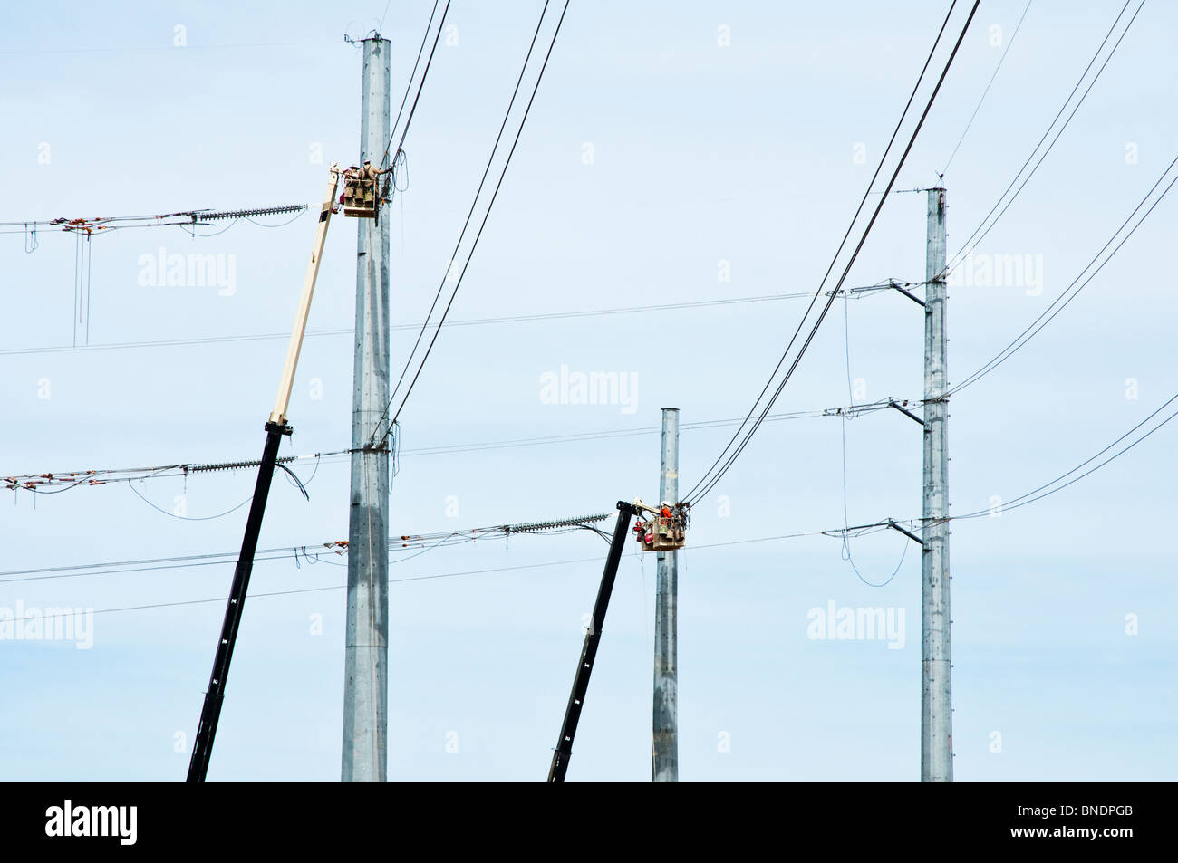 Quattro lavoratori edili in un cherry picker ceste il lavoro su una nuova linea di trasmissione di potenza. Foto Stock