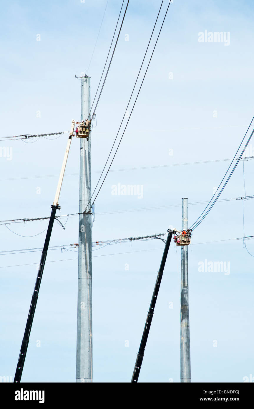 Quattro lavoratori edili in un cherry picker ceste il lavoro su una nuova linea di trasmissione di potenza. Foto Stock