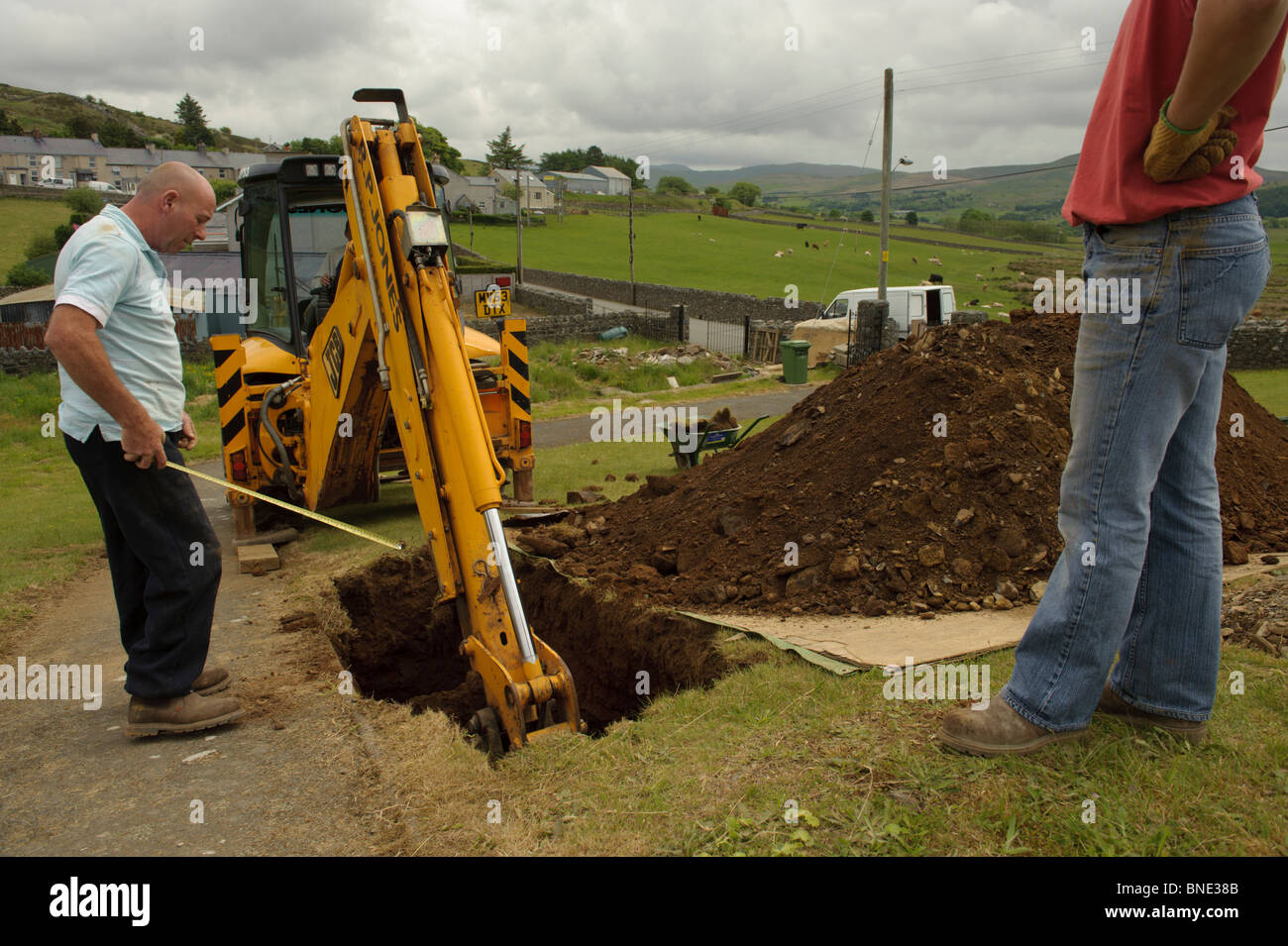 Contraente tomba di scavo con un escavatore JCB in Steshon villaggio nei pressi di Trawsfynydd, Parco Nazionale di Snowdonia, Gwynedd North Wales UK Foto Stock