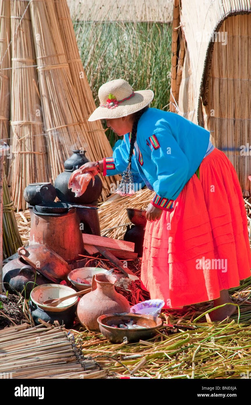 Una donna in abito tradizionale cucinare un pasto sull'isola galleggiante di Uros nel Lago Titicaca, Perù, Sud America. Foto Stock