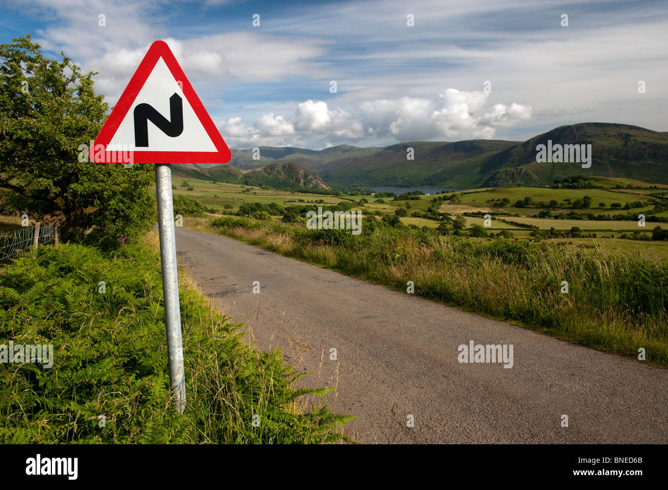 Cartello stradale sulla stretta strada rurale di avvertimento di strada tortuosa in anticipo. Foto Stock