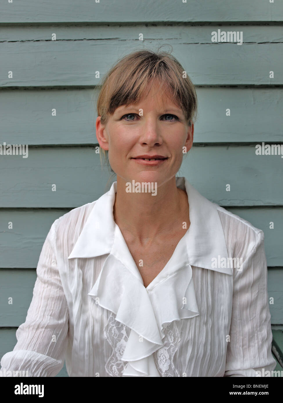 Modello di donna femmina in bianco frilly blusa con capelli tirati indietro guardando direttamente nel ritratto della fotocamera Foto Stock