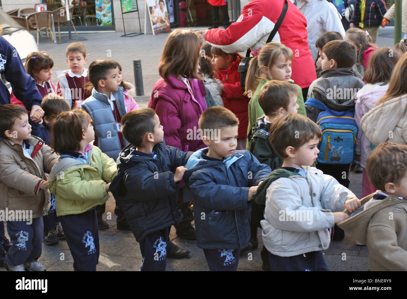 Adulti organizzare i giovani della scuola i bambini (5-6 anni) per tenere ciascun altri cofani per attraversare la strada insieme in modo sicuro Foto Stock