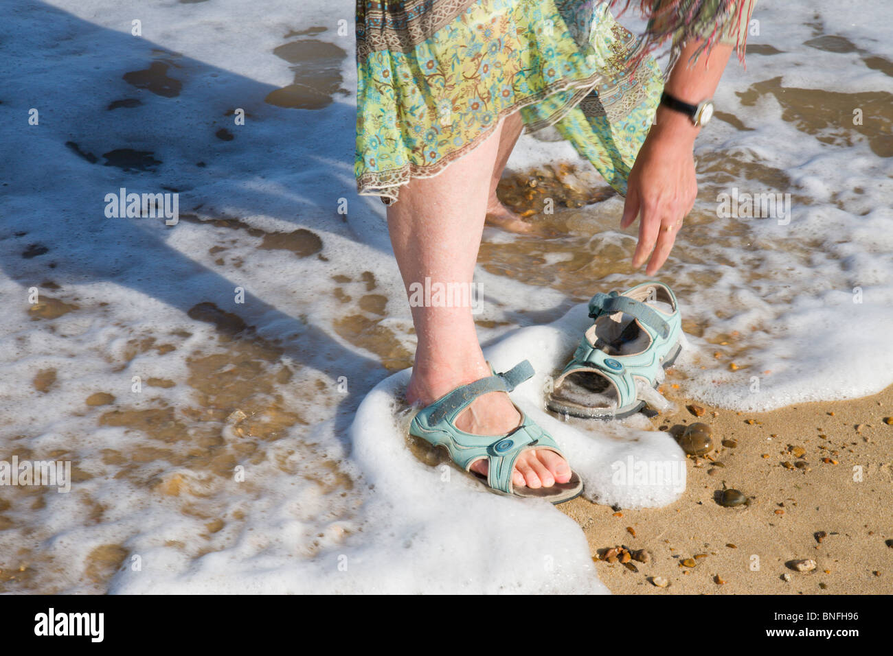 Una donna messa in sandali al mare waters edge. Foto Stock