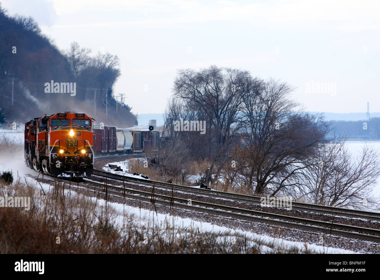 Una ferrovia BNSF treno merci rotoli lungo il fiume Mississippi in una fredda giornata invernale. Foto Stock