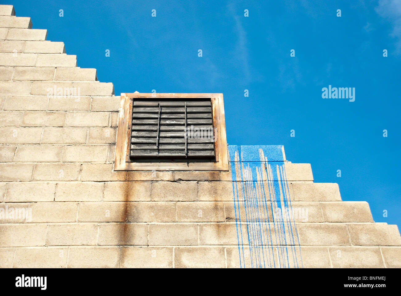 Parzialmente smantellato in calcestruzzo parete in mattoni con la vernice blu accento, una defunta - sfiato contro il cielo blu. Foto Stock