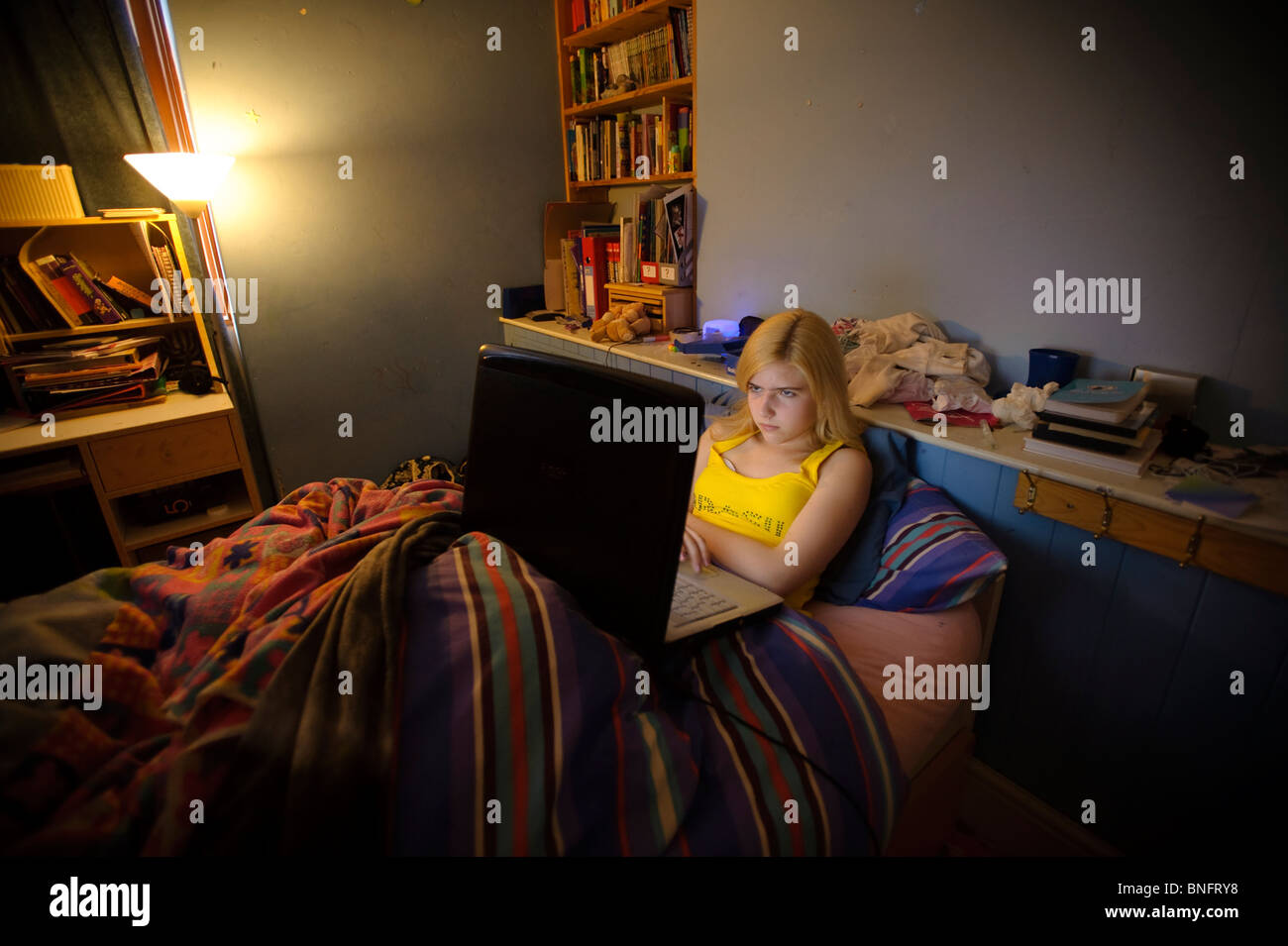 A quindici anni ragazza adolescente usando il suo computer portatile per chattare con i suoi amici di Facebook online dalla sua camera da letto, REGNO UNITO Foto Stock
