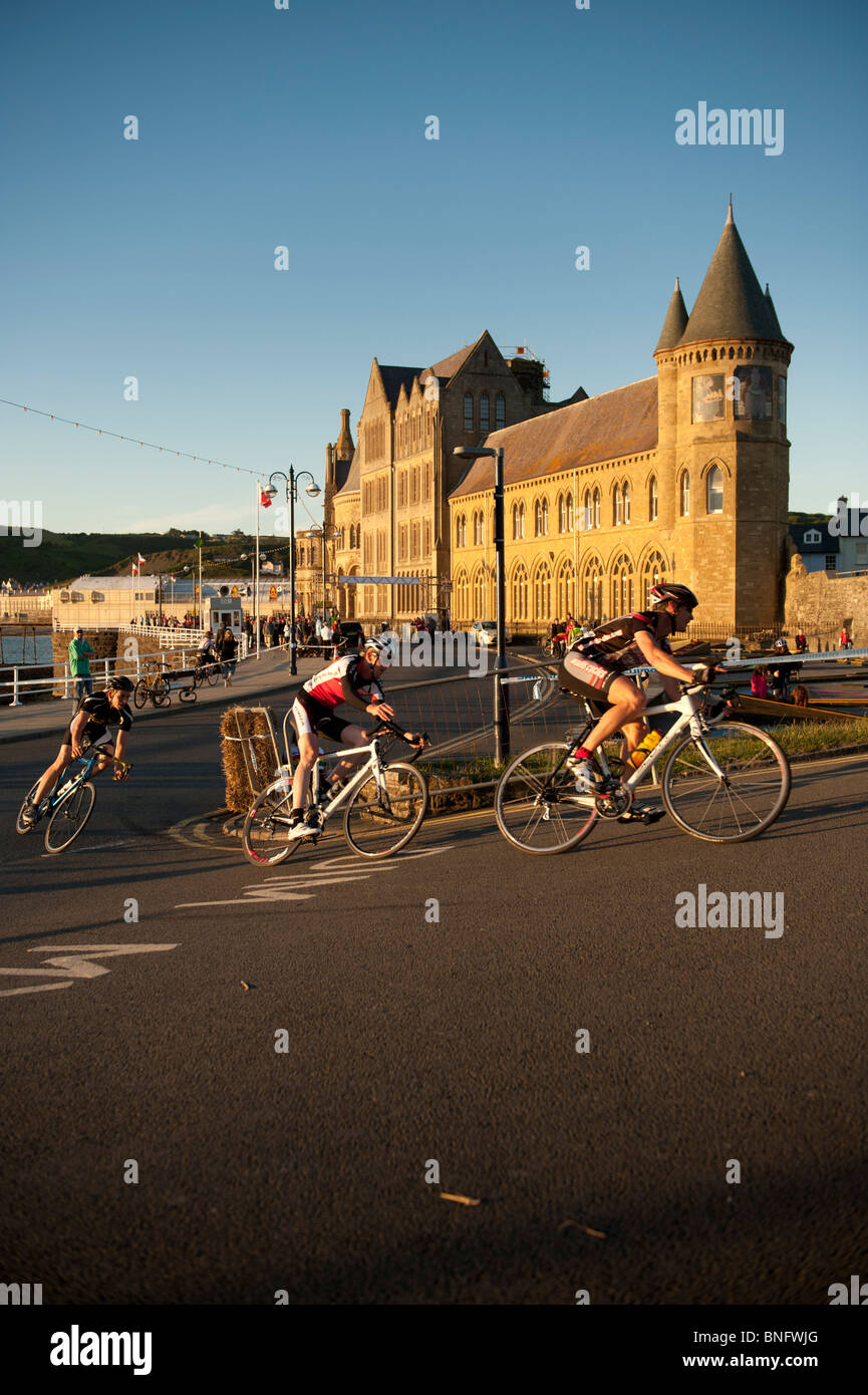 I ciclisti per competere in una gara in giro per le strade di Aberystwyth Wales UK, palazzo universitario in background Foto Stock