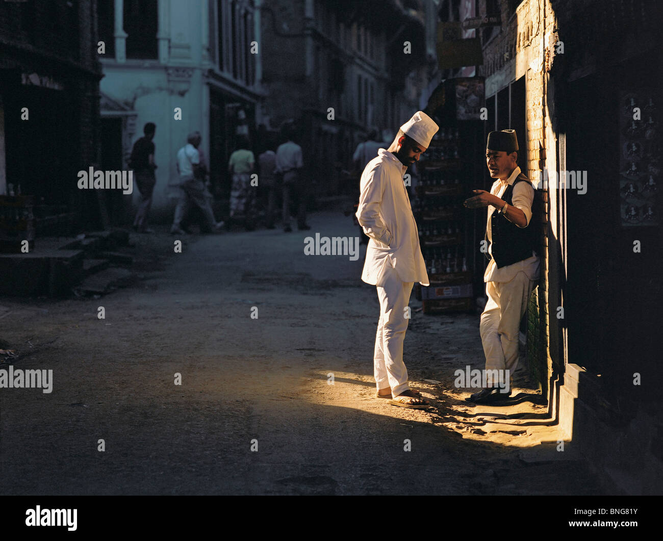 Due uomini in chat in una patch di luce del sole in una Kathmandu backstreet, Kathmandu, Nepal Foto Stock