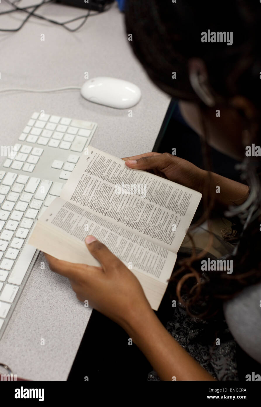 Femmina studente afro-americano cerca parola nel dizionario mentre si lavora sul computer a Manor New Tech High School Foto Stock