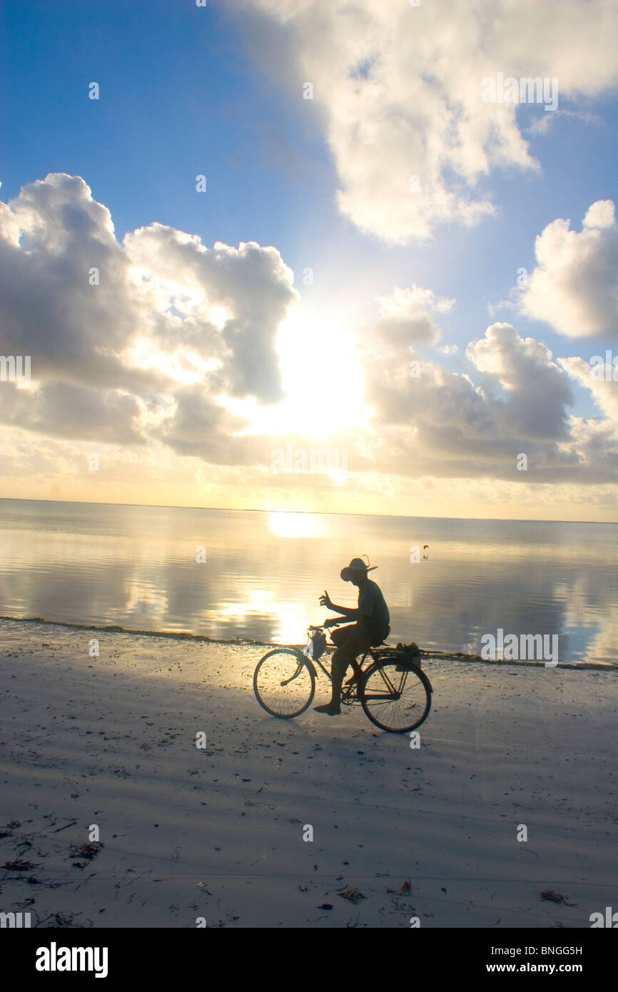 Silhouette del pescatore salutando mentre escursioni in bicicletta lungo la spiaggia di sunrise, Bwejuu, Zanzibar, Tanzania Foto Stock