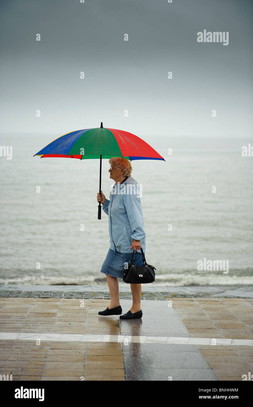 Una donna che cammina lungo Aberystwyth promenade sotto la pioggia su un luglio bagnato estate pomeriggio, Wales UK Foto Stock