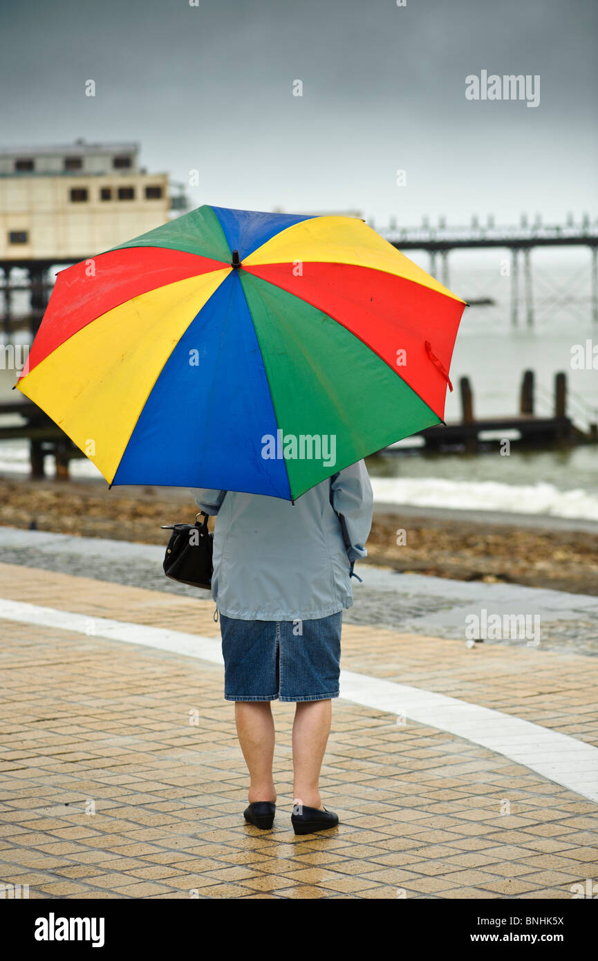 Vista posteriore di una donna il ricovero sotto un ombrellone in Aberystwyth promenade sotto la pioggia luglio bagnato estate pomeriggio, Wales UK Foto Stock