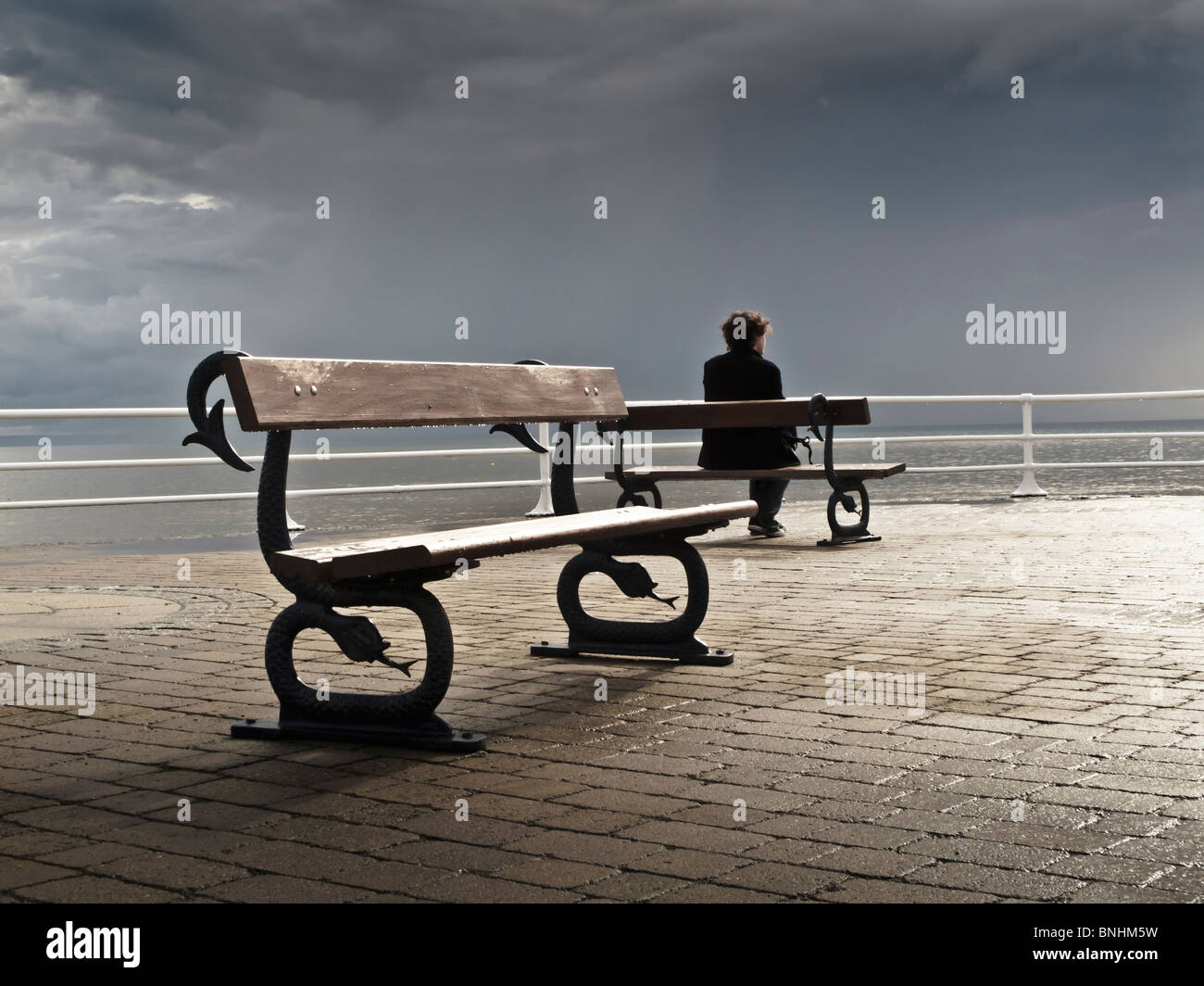 Un uomo seduto da solo su una panchina sul lungomare, grigio nuvoloso luglio pomeriggio estivo, Aberystwyth Wales UK Foto Stock
