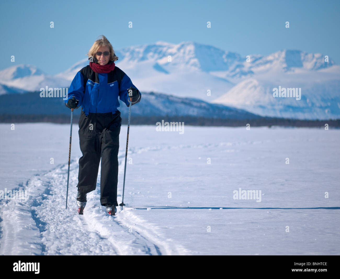 Una donna lo sci nella sua fourties fa il suo modo sopra la congelati Kaalasjärvi lago di fronte al massiccio del Kebnekaise a Kiruna. Foto Stock