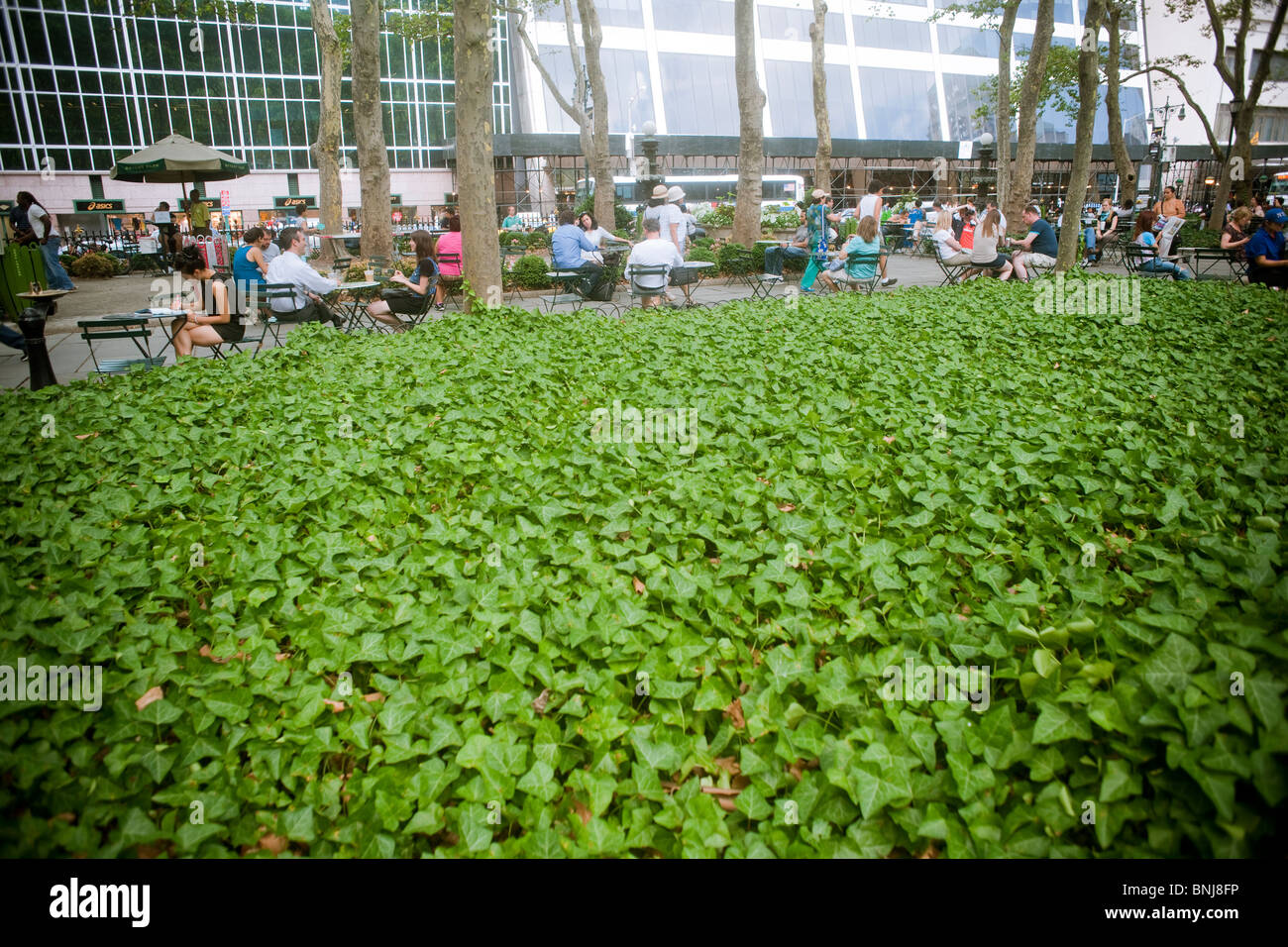 I visitatori al Bryant Park di New York rilassarsi all'ombra sotto gli alberi per battere il calore. Foto Stock