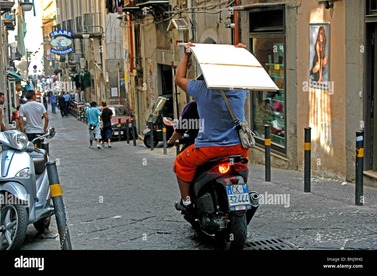 Una scena di strada a Napoli Italia - un passeggero posteriore porta una lastra di cartongesso sulla sua testa Foto Stock