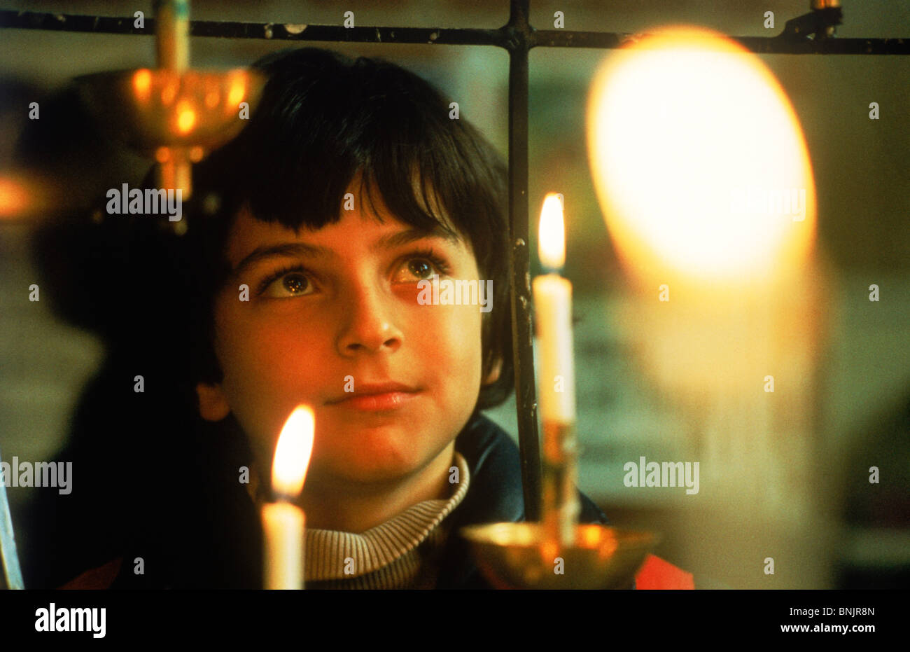 Ragazzo giovane staring al lume di candela durante il servizio in chiesa Foto Stock
