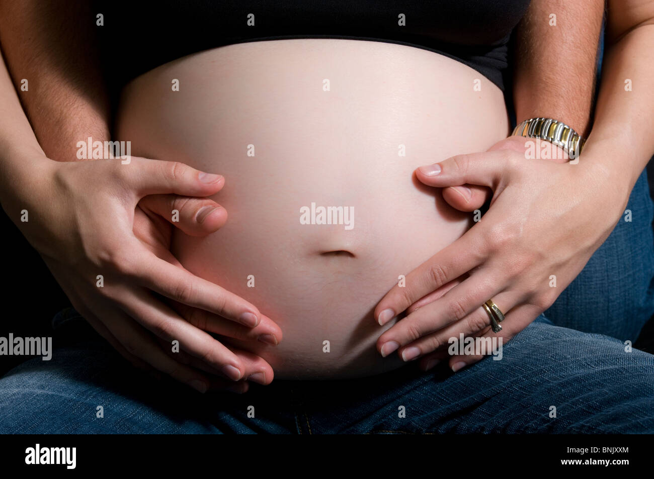La gravidanza di una pancia getting abbracciato dalla madre e padre, solo la pancia e le mani e le braccia mostrato. Foto Stock