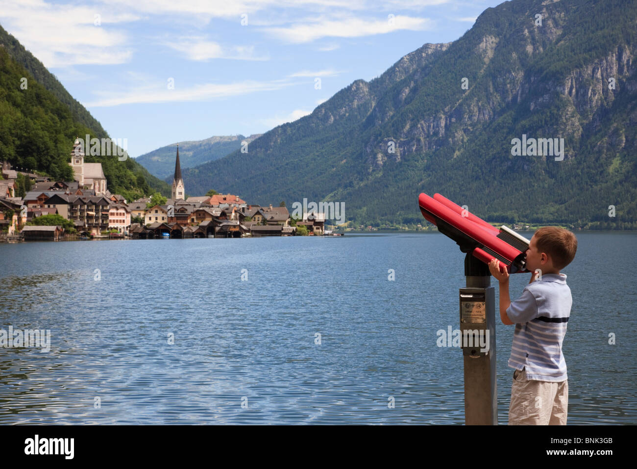 Ragazzo che guarda attraverso un telescopio per il patrimonio culturale mondiale villaggio sul lago Hallstattersee. Hallstatt, Salzkammergut, Austria. Foto Stock