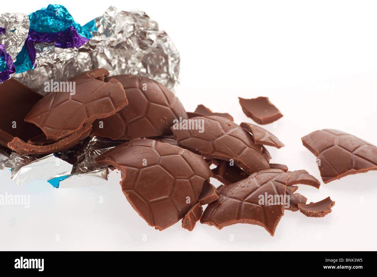 Close-up di pezzi rotti del cioccolato al latte uovo di pasqua con argento e blu involucro in foglio su sfondo bianco Foto Stock