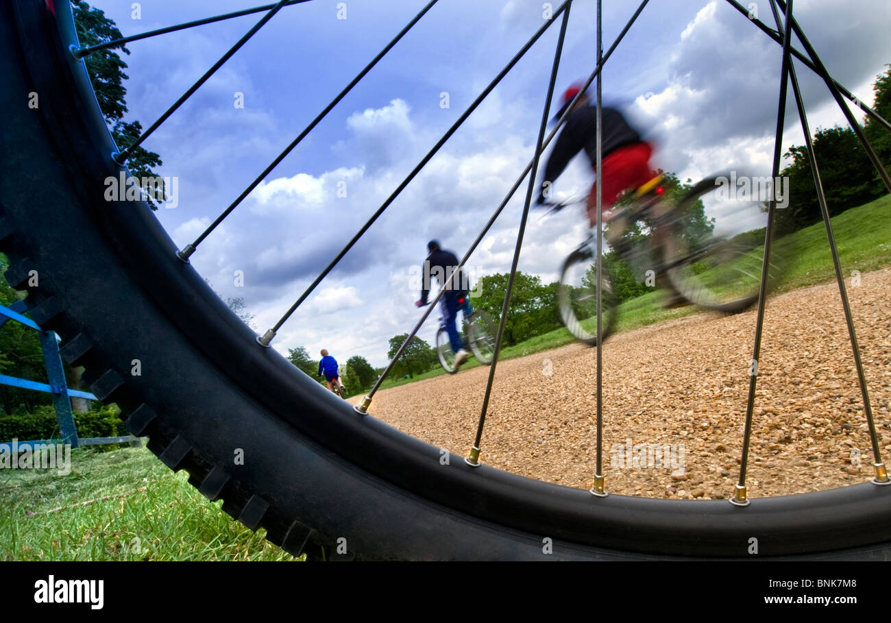 I ciclisti percorso in bicicletta all'aperto godendo di una corsa in un parco locale visto attraverso la ruota di bicicletta e raggi Foto Stock