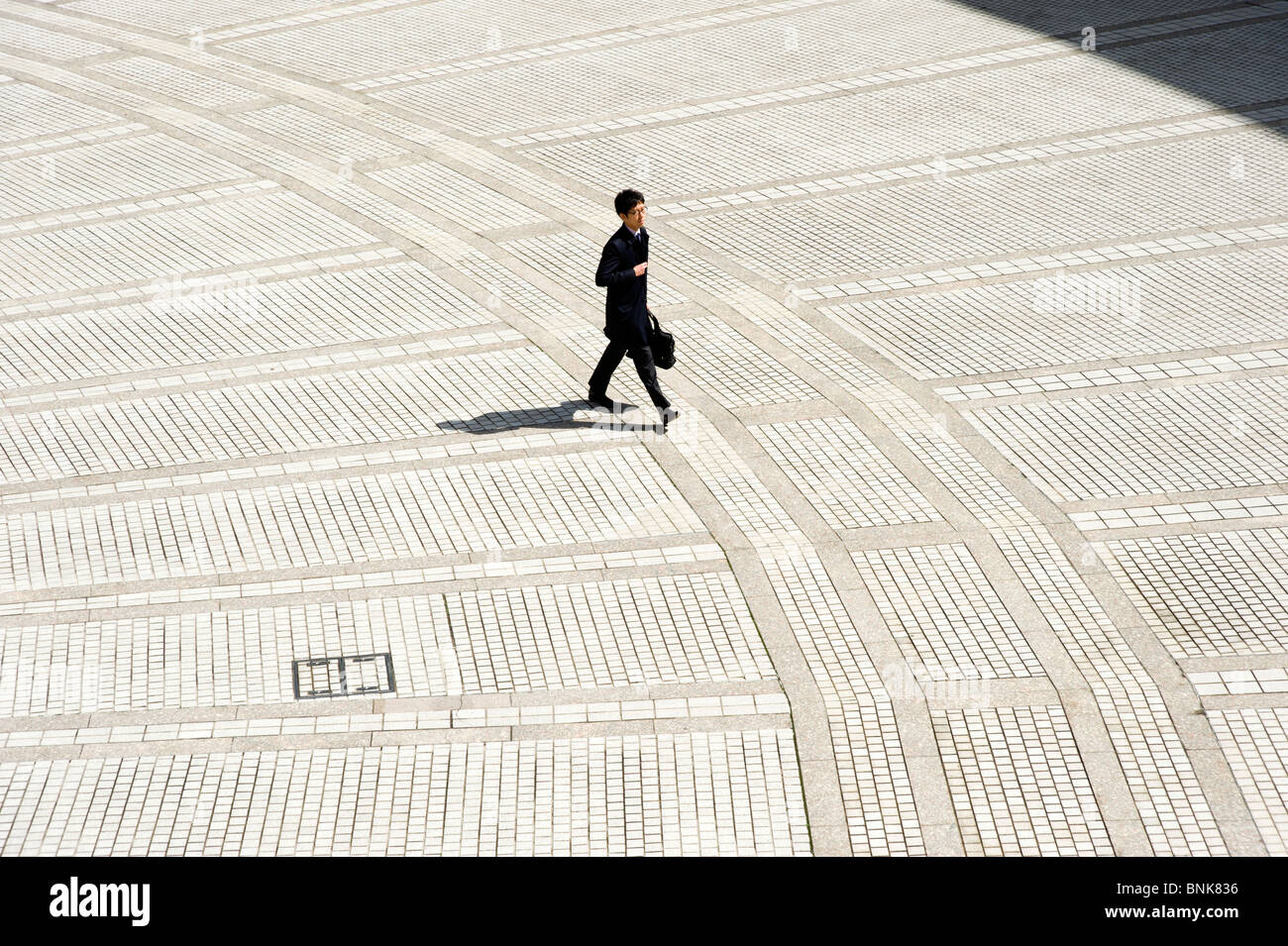 Imprenditore attraversare piazzale vuoto in Shinjuku, Tokyo, Giappone Foto Stock