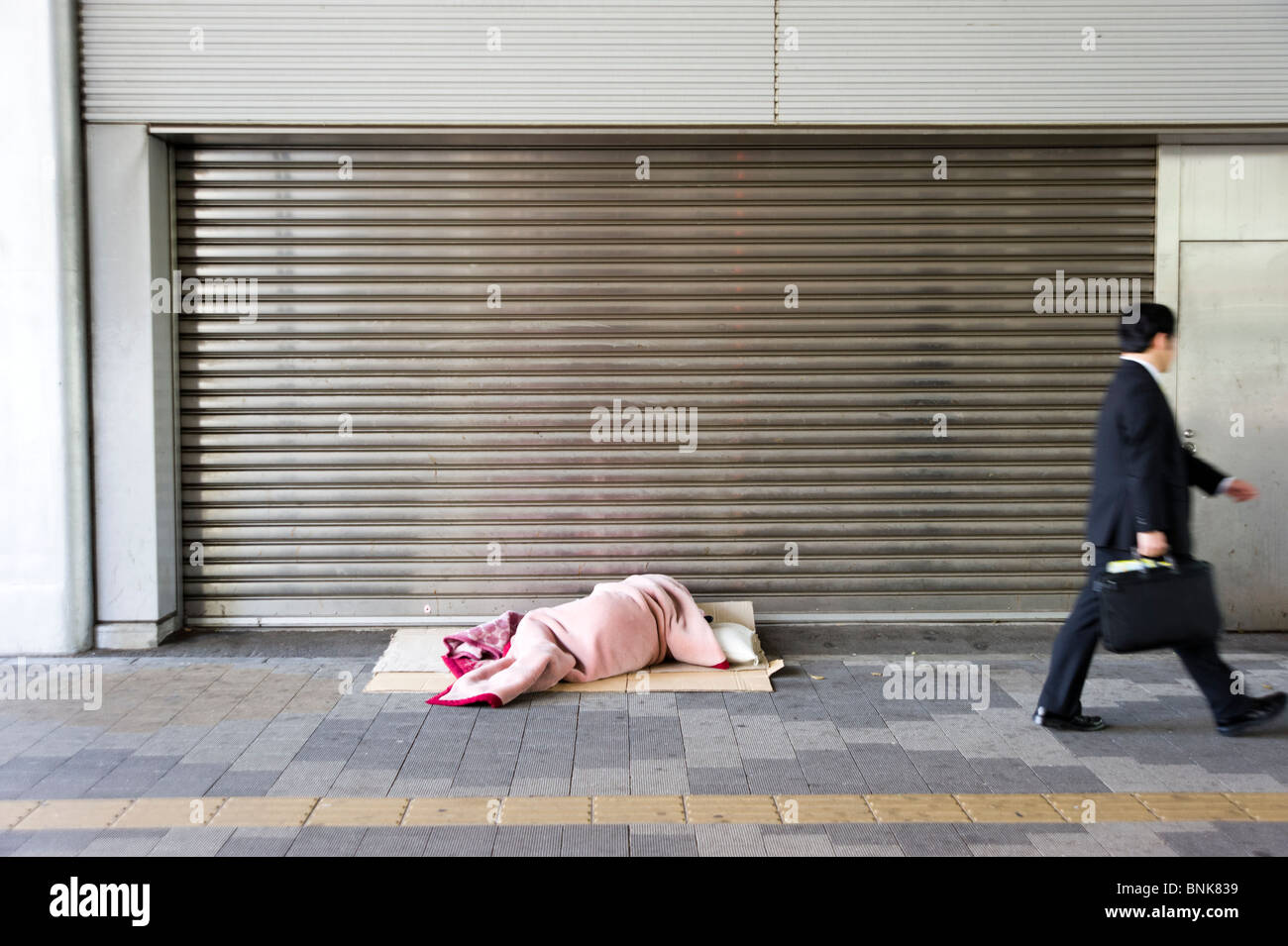 Senzatetto uomo dorme in modo irregolare a Shinjuku mentre cammina l'uomo passato, Tokyo, Giappone Foto Stock