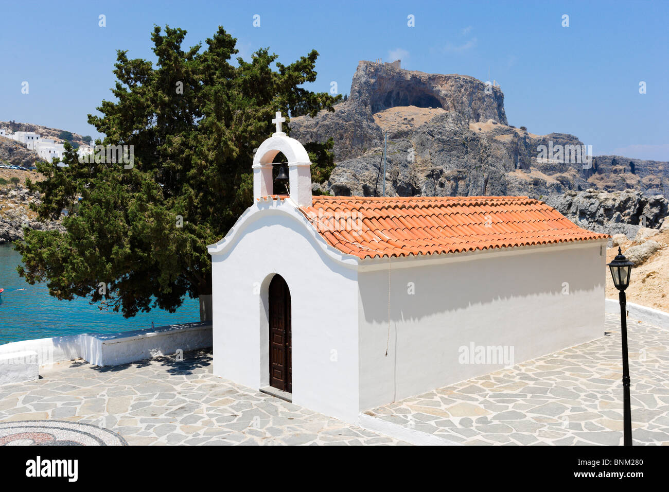 La cappella dipinta di bianco a St Paul Bay con l'acropoli dietro, Lindos, Rodi, Grecia Foto Stock