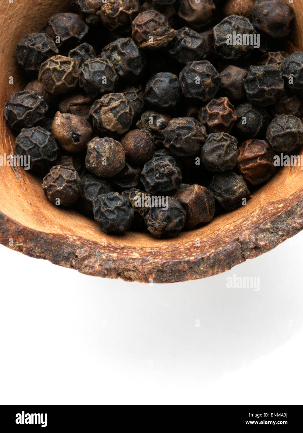 Close up di pepe nero in una ciotola di legno su uno sfondo bianco Foto Stock