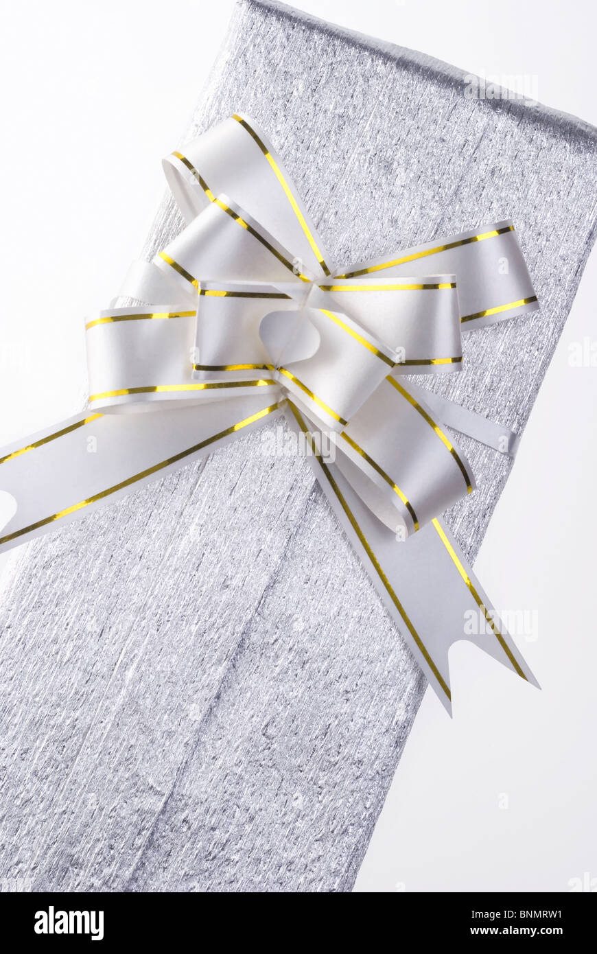 Un pacco avvolto in argento di carta metallizzata, con un grande filtro bow tie, su bianco. Foto Stock