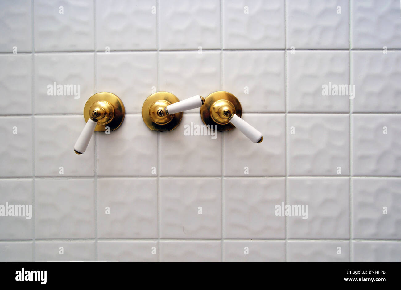 Tre golden shower valvola gestisce ona grande bianco piastrella vuota sala da bagno con doccia Foto Stock