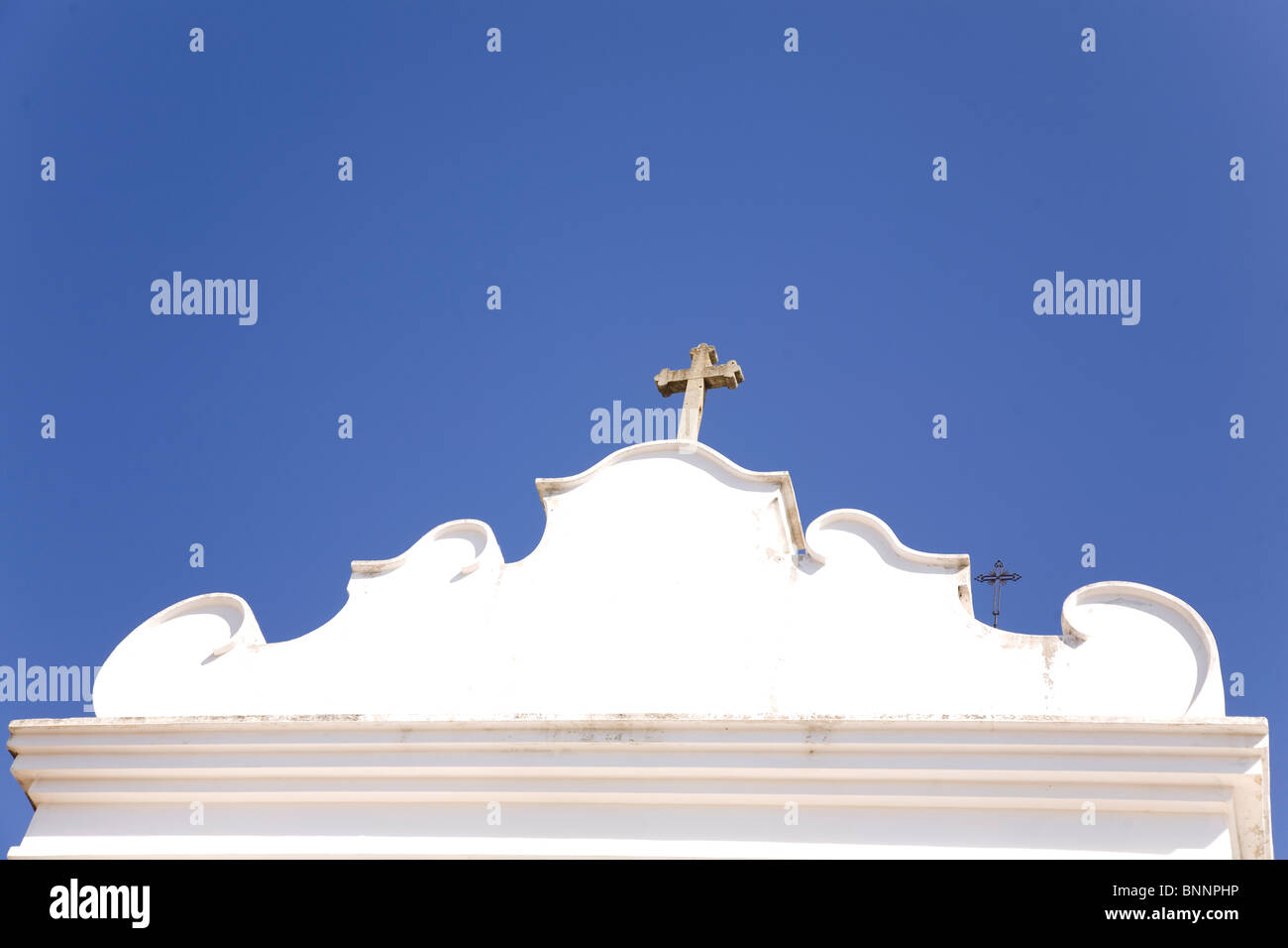 Un crocifisso sorge evidenziato contro un cielo azzurro intenso su un dipinto di bianco in stile barocco nel muro della città di Faro, Portogallo. Foto Stock