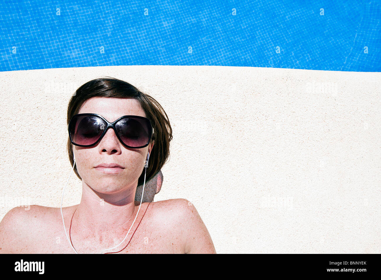 Colpo di un attraente marrone donna dai capelli vicino alla piscina con i suoi auricolari Foto Stock