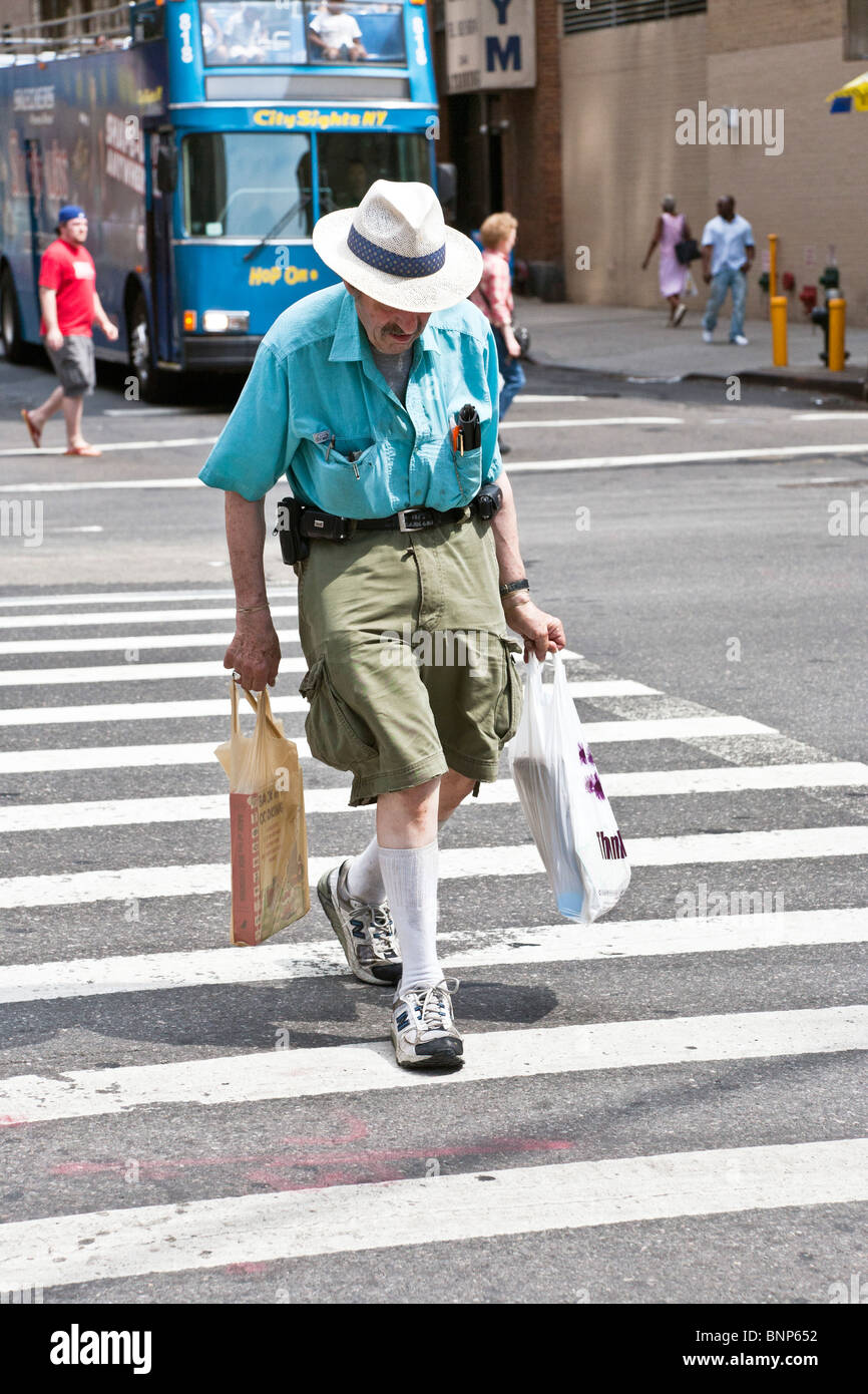 Il vecchio gentleman indossando Elegante cappello di paglia colorata a manica corta shirt & cargo pantaloncini con tasche di spanciamento hurries attraverso street Foto Stock