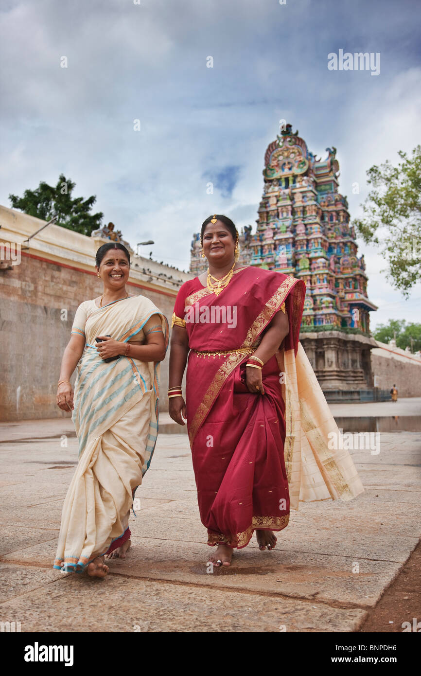 Due donna indiana nel tradizionale rosso e crema Sari a piedi a un tempio per offrire grazie Foto Stock