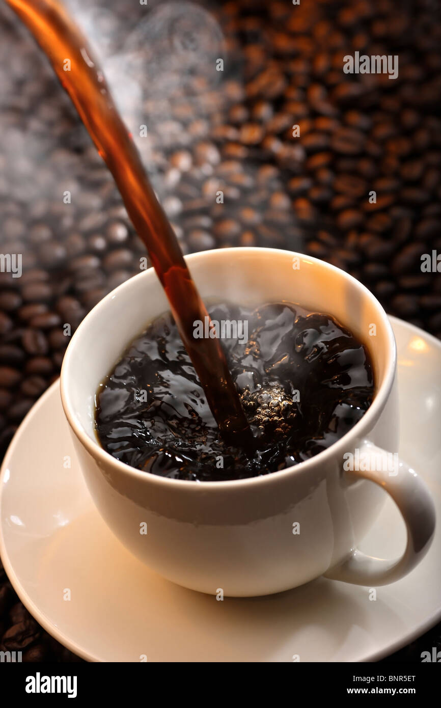 Versando una tazza di cottura a vapore tradizionale caffè caldo contro il caffè-sfondo bean Foto Stock