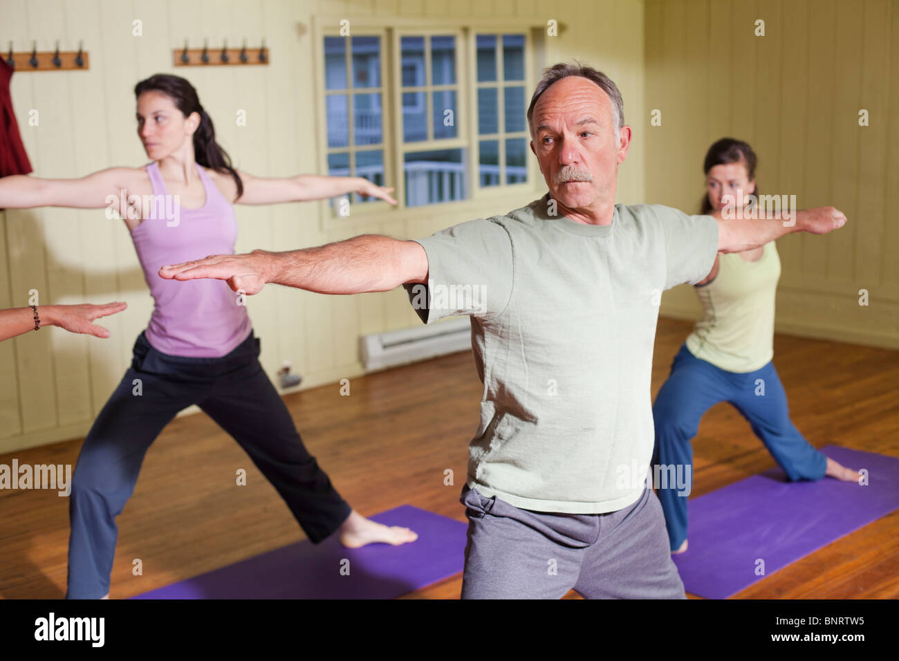 Due giovani donne e un uomo più anziano pratica yoga in un piccolo studio. Foto Stock